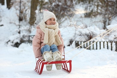 Photo of Cute little girl enjoying sledge ride through snow in winter park