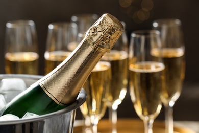 Photo of Bottle of champagne in bucket with ice and glasses on blurred background, closeup. Space for text