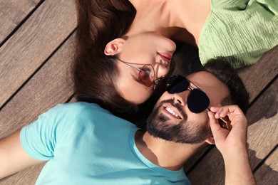 Photo of Beautiful woman and handsome smiling man in sunglasses on wooden deck outdoors, above view