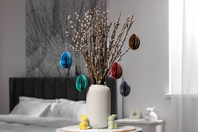 Photo of Beautiful pussy willow branches with paper eggs in vase and bunny figures on table at home. Easter decor