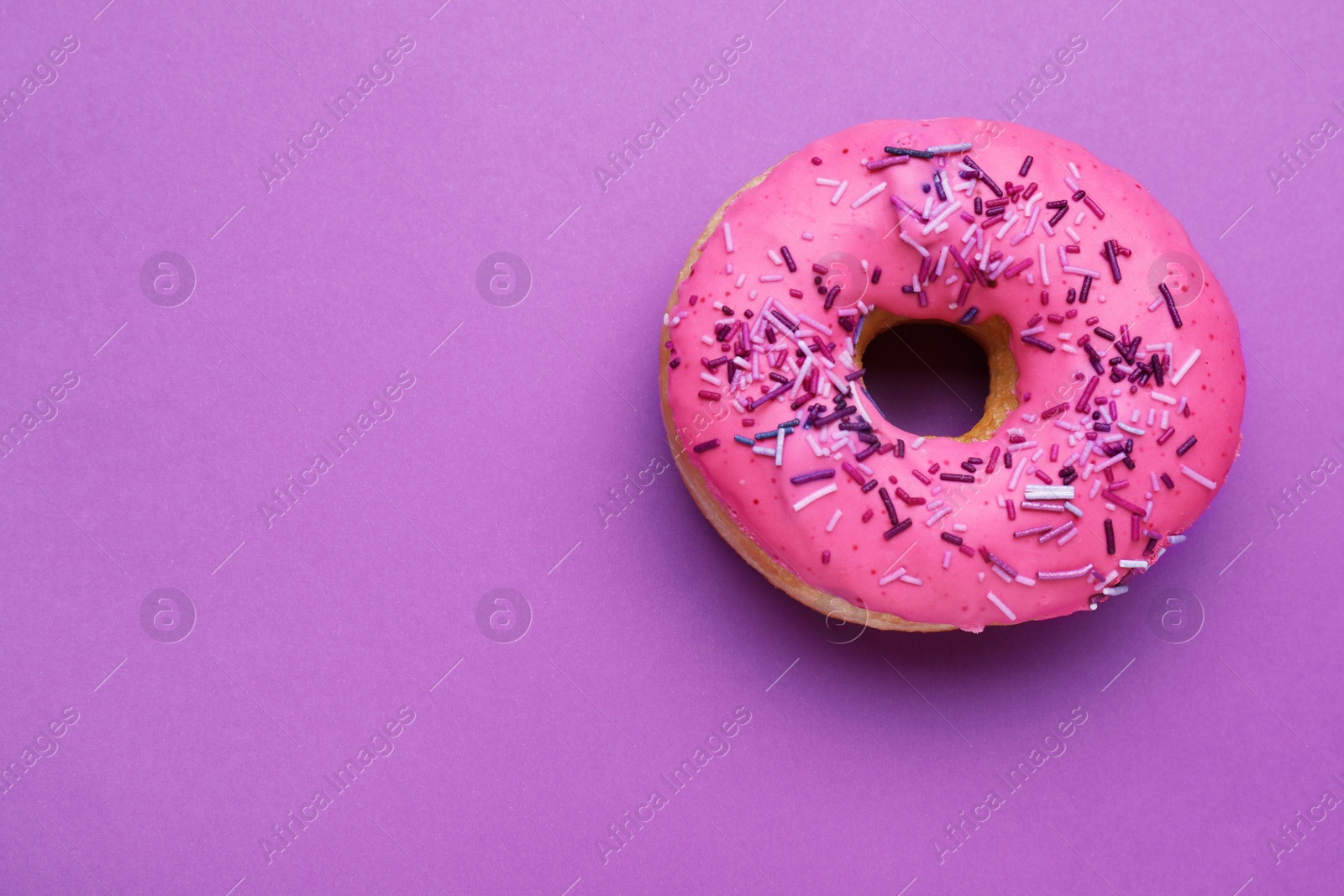 Photo of Sweet glazed donut decorated with sprinkles on purple background, top view and space for text. Tasty confectionery