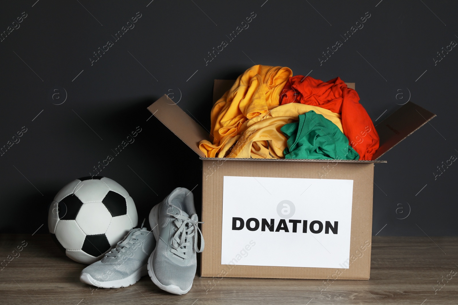 Photo of Donation box with clothes, shoes and soccer ball on table against black background