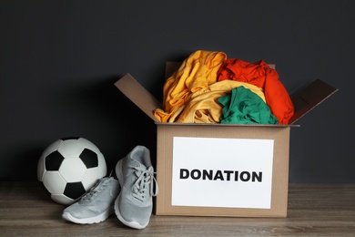 Donation box with clothes, shoes and soccer ball on table against black background