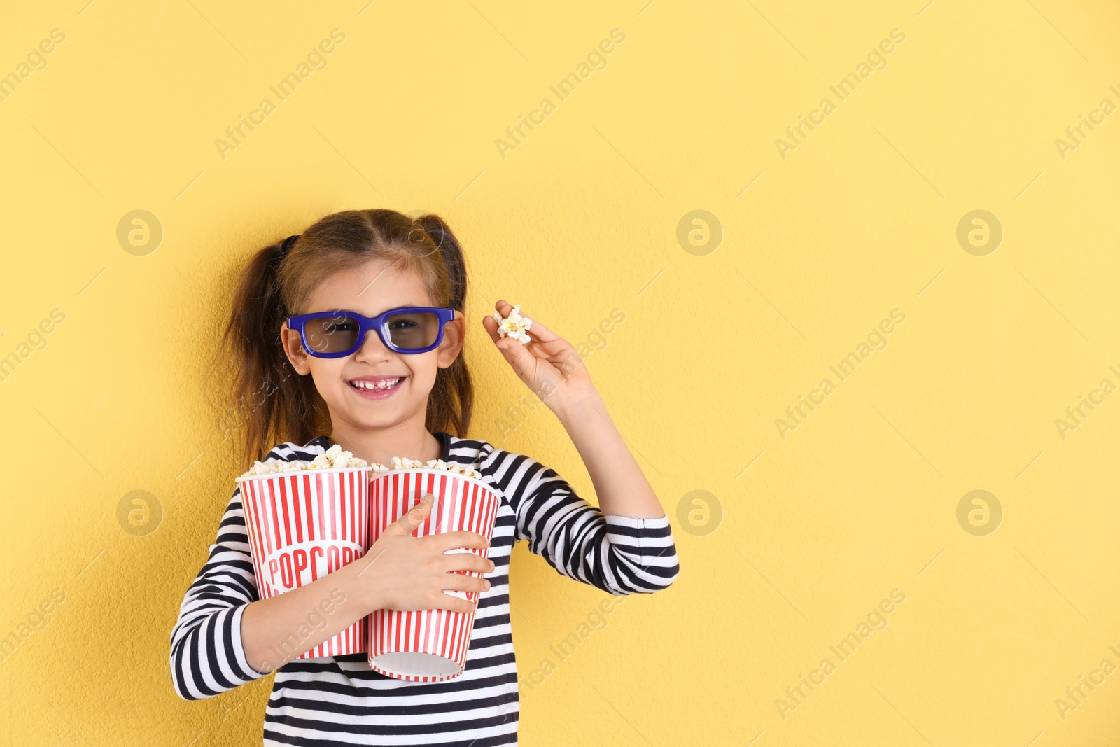 Photo of Cute little girl with popcorn and glasses on color background. Space for text