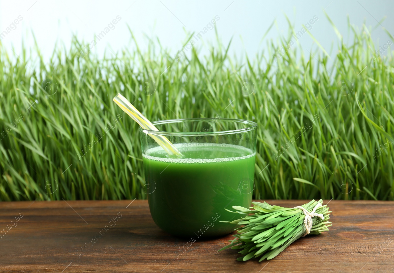 Glass of juice on wooden table near fresh wheat grass Photo of Glass of juice on wooden table near fresh wheat grass