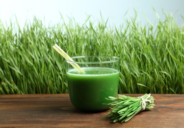 Photo of Glass of juice on wooden table near fresh wheat grass