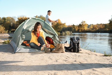 Photo of Young woman lacing shoe near tent outdoors, space for text. Sleeping bag and camping equipment