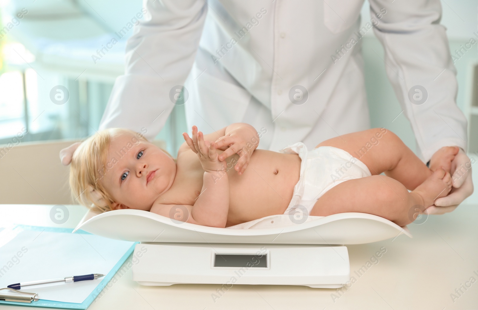 Photo of Pediatrician weighting baby on scale in hospital. Healthy growth