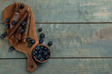 Photo of Delicious fruit leather rolls and blueberries on blue wooden table, flat lay. Space for text