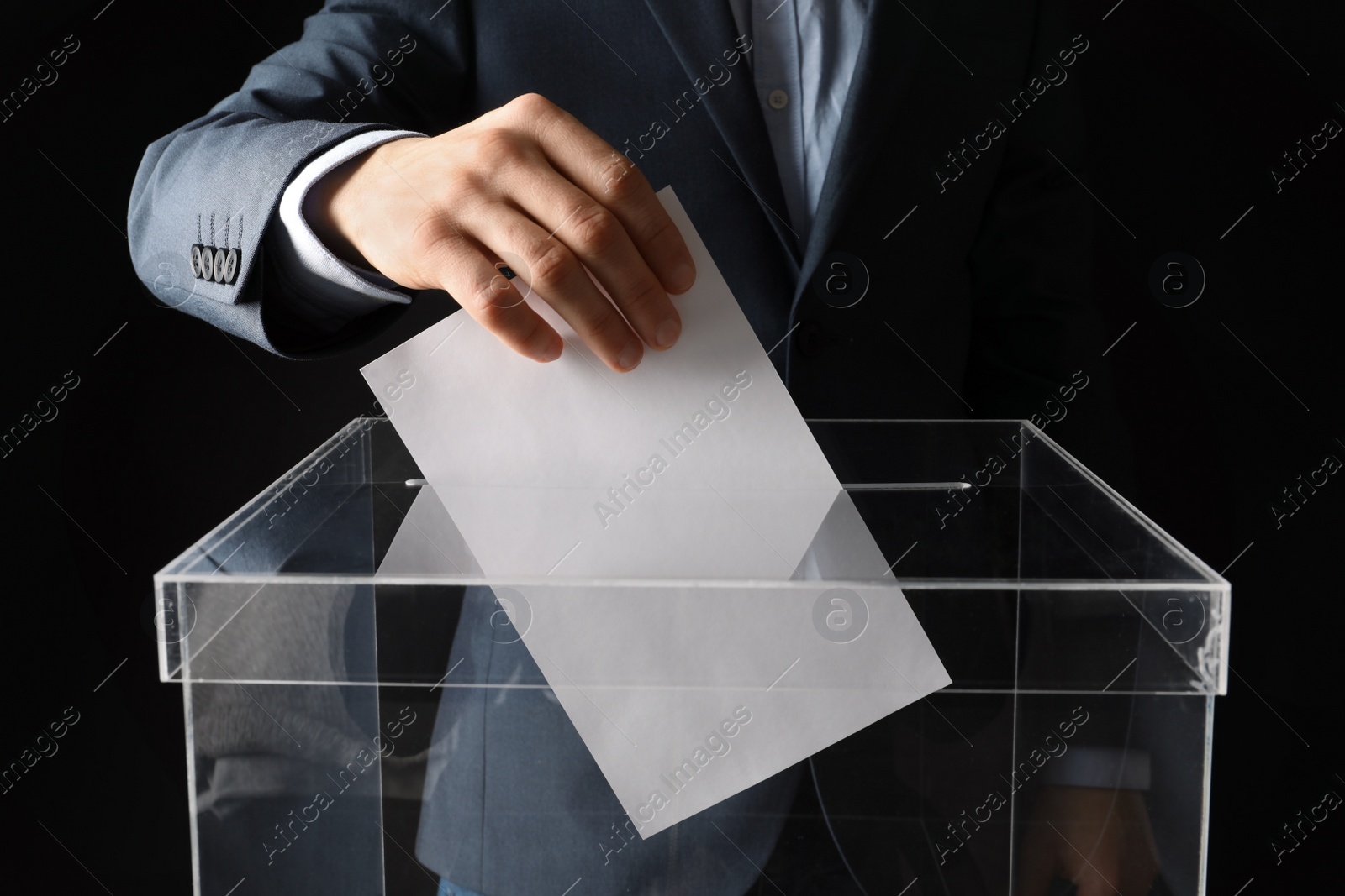 Photo of Man putting his vote into ballot box on black background, closeup