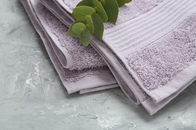 Photo of Violet terry towel and eucalyptus branch on grey table, closeup