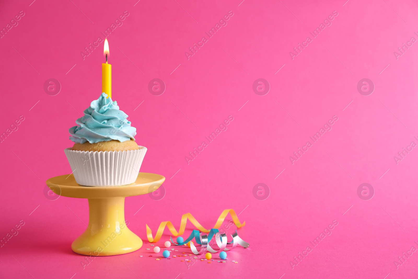 Photo of Birthday cupcake with burning candle and streamers on pink background. Space for text
