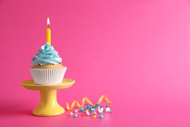 Photo of Birthday cupcake with burning candle and streamers on pink background. Space for text