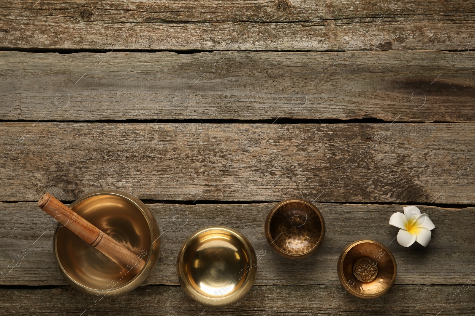 Photo of Golden singing bowls, mallet and flower on wooden table, flat lay. Space for text