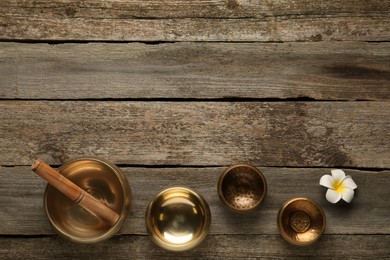 Photo of Golden singing bowls, mallet and flower on wooden table, flat lay. Space for text