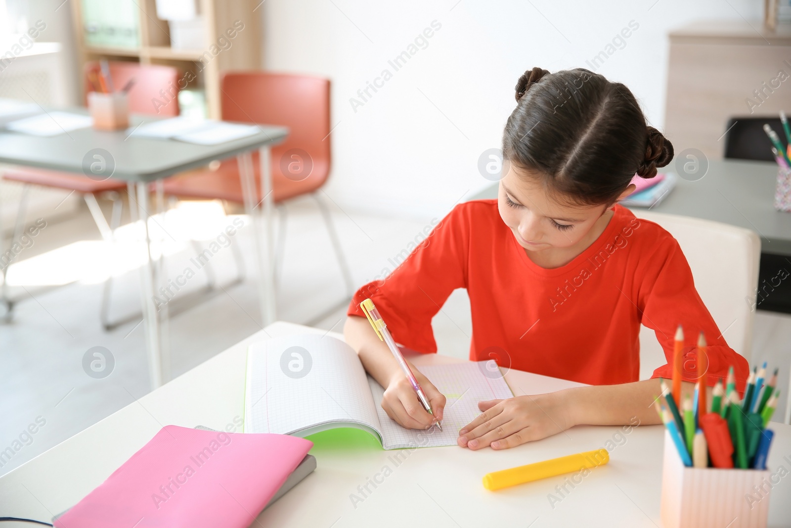 Photo of Cute little child doing assignment at desk in classroom. Elementary school