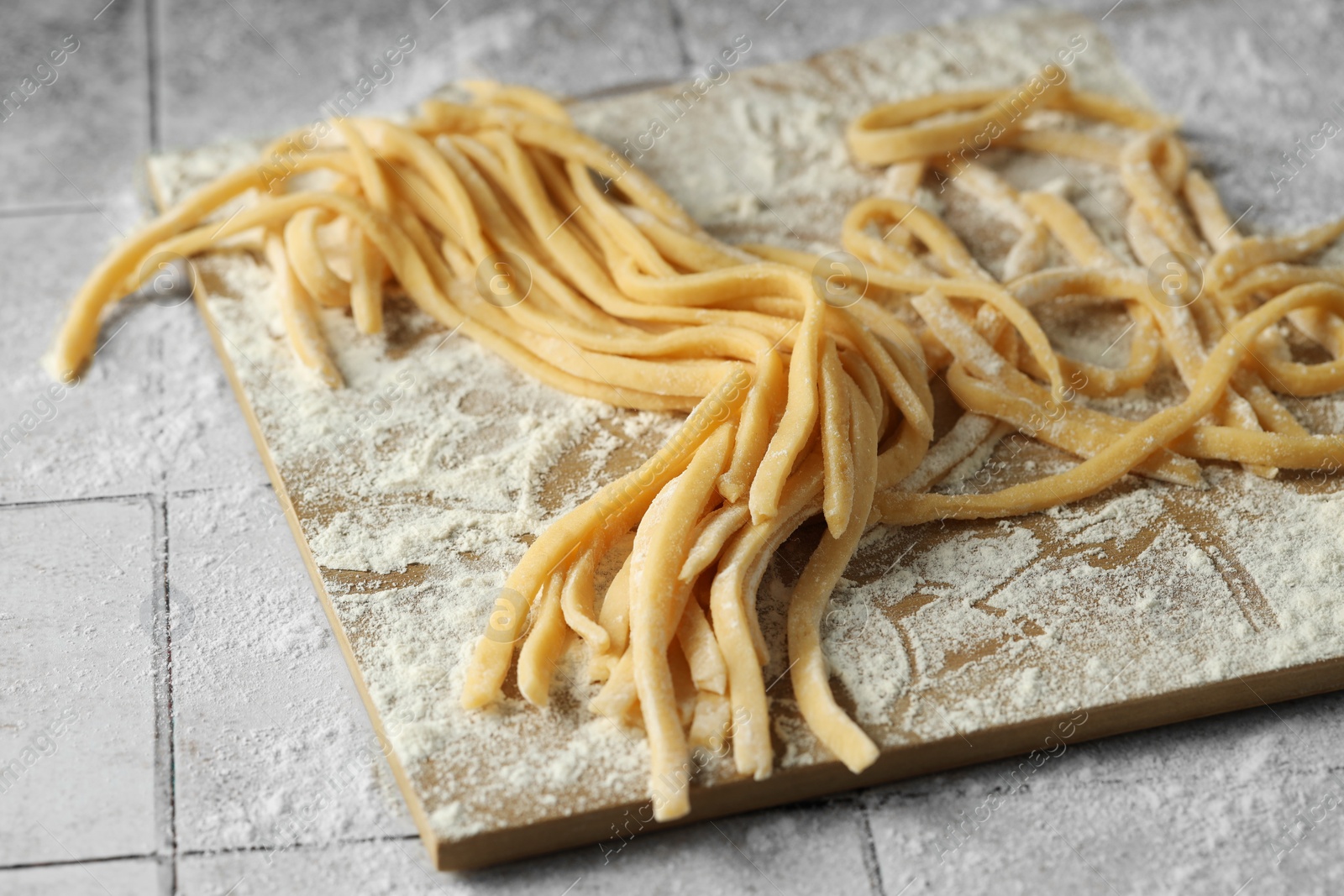 Photo of Raw homemade pasta and flour on white tiled table