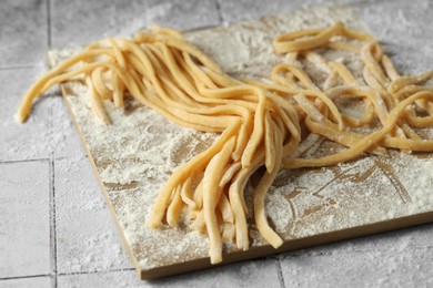 Photo of Raw homemade pasta and flour on white tiled table