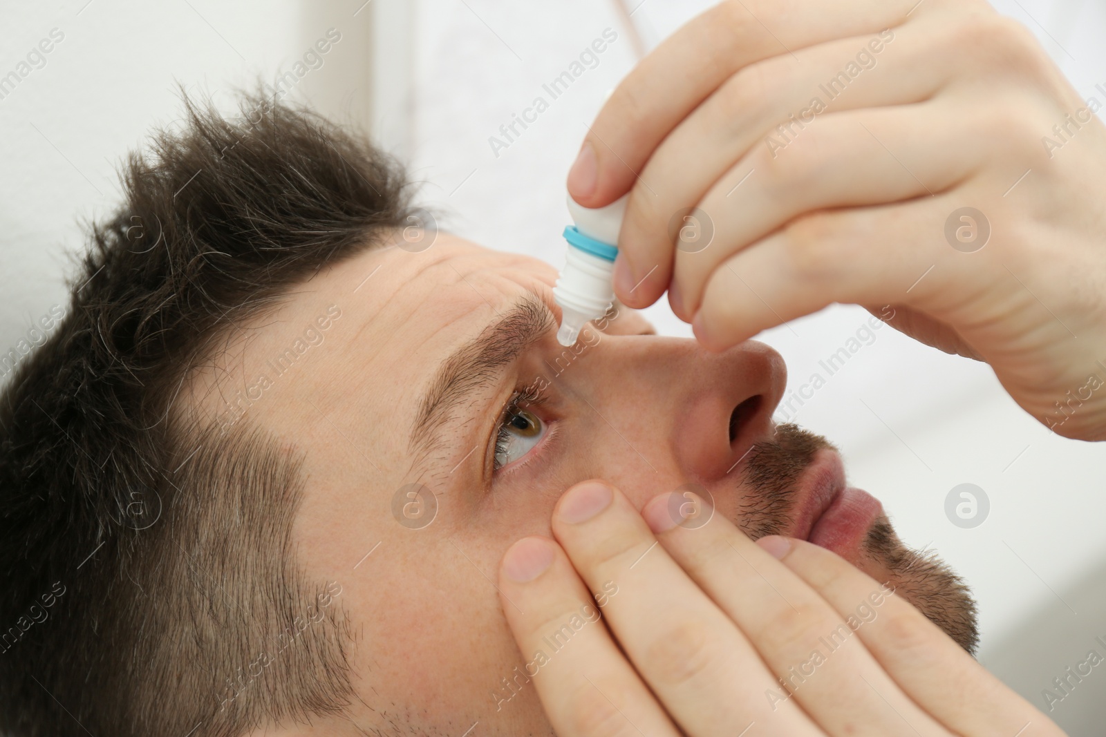 Photo of Man using eye drops indoors, closeup view