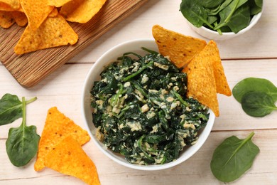 Photo of Tasty spinach dip with eggs in bowl and nachos chips on light wooden table, top view