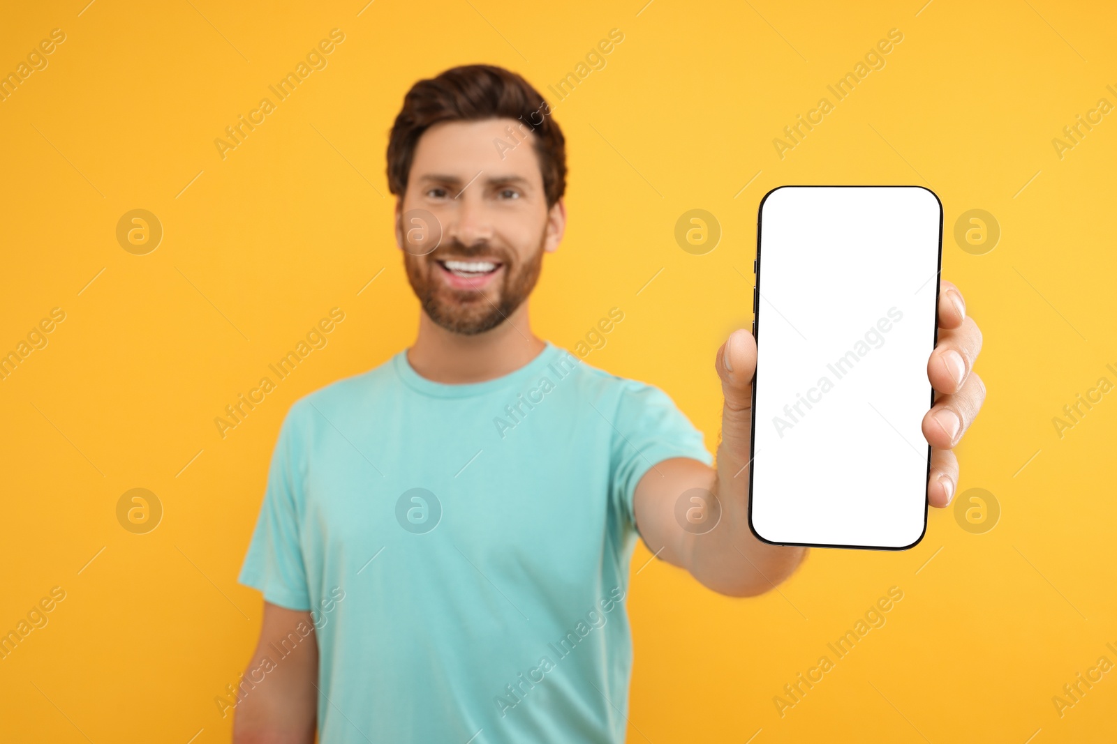 Photo of Handsome man showing smartphone in hand on yellow background, selective focus. Mockup for design