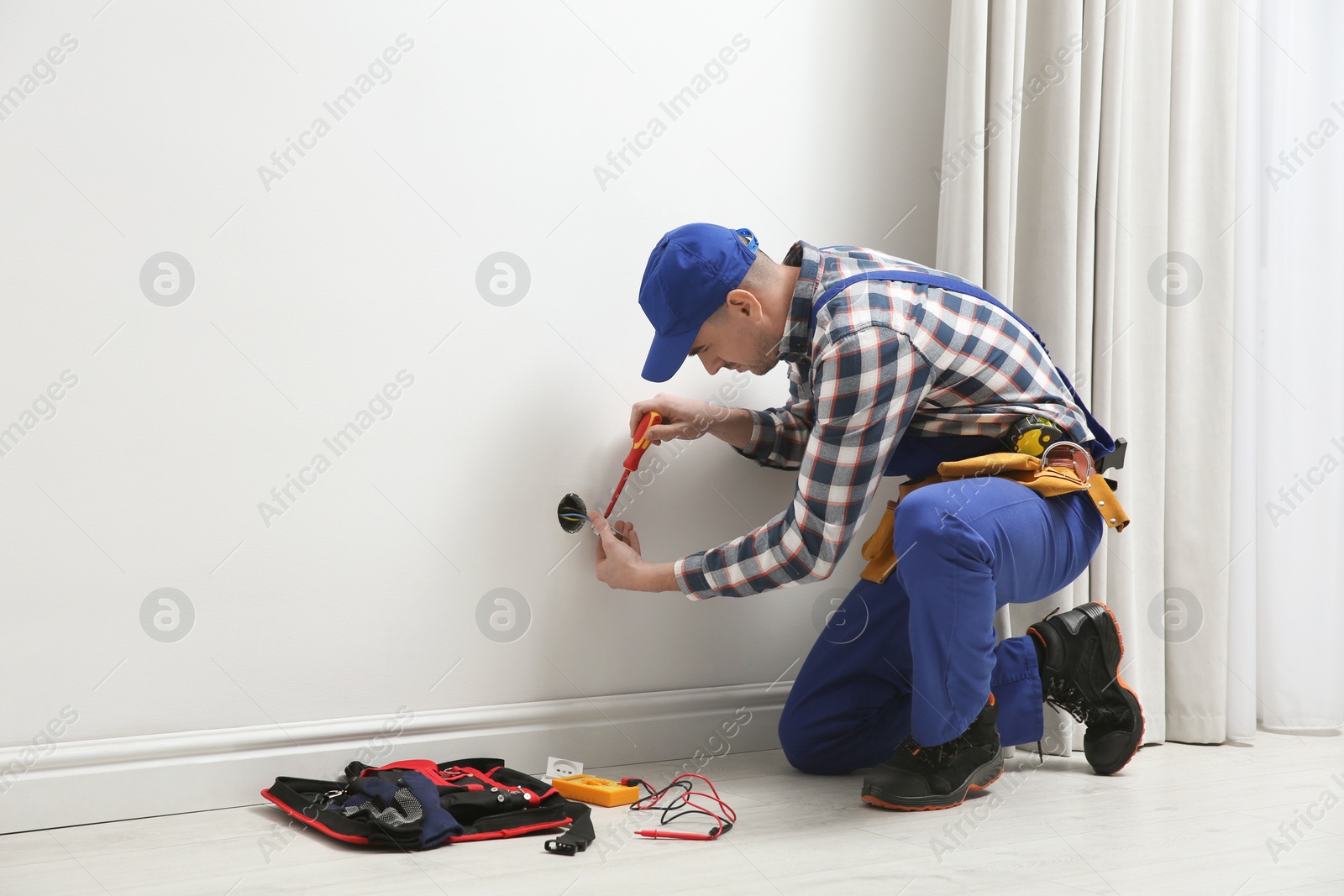 Photo of Electrician with screwdriver repairing power socket indoors