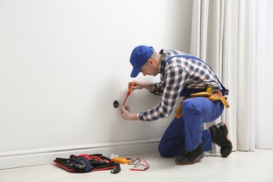 Photo of Electrician with screwdriver repairing power socket indoors