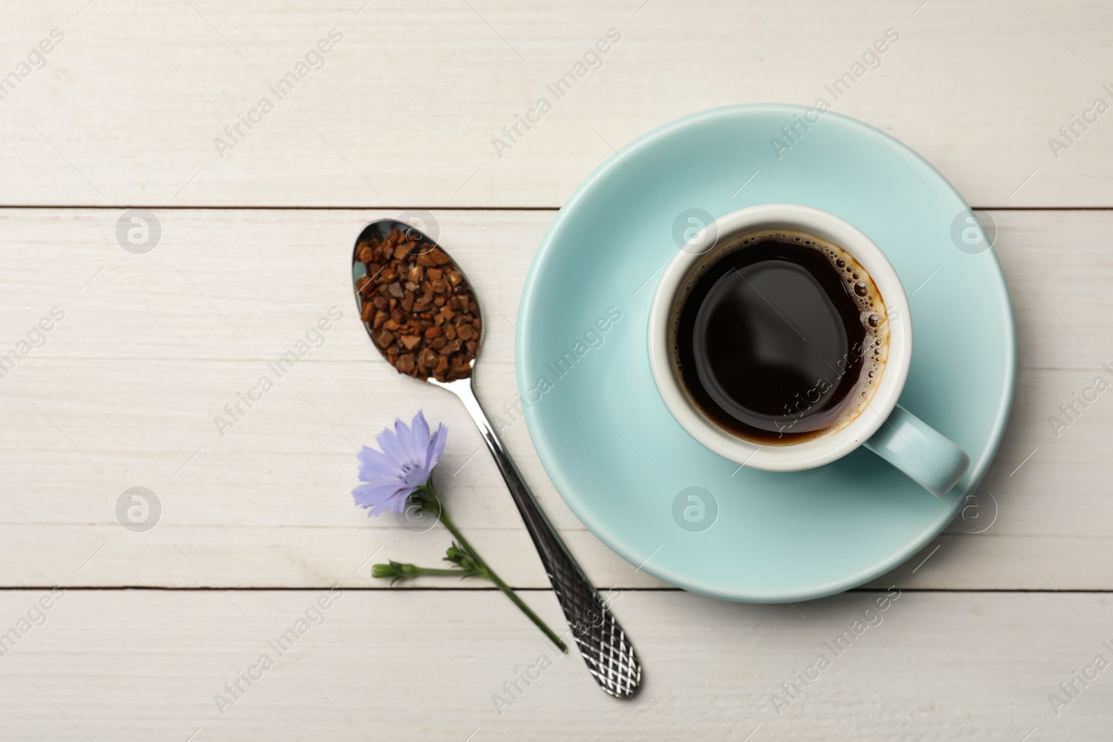 Photo of Cup of delicious chicory drink, granules and flower on white wooden table, flat lay