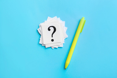Heap of paper notes with question marks and pen on light blue background, flat lay