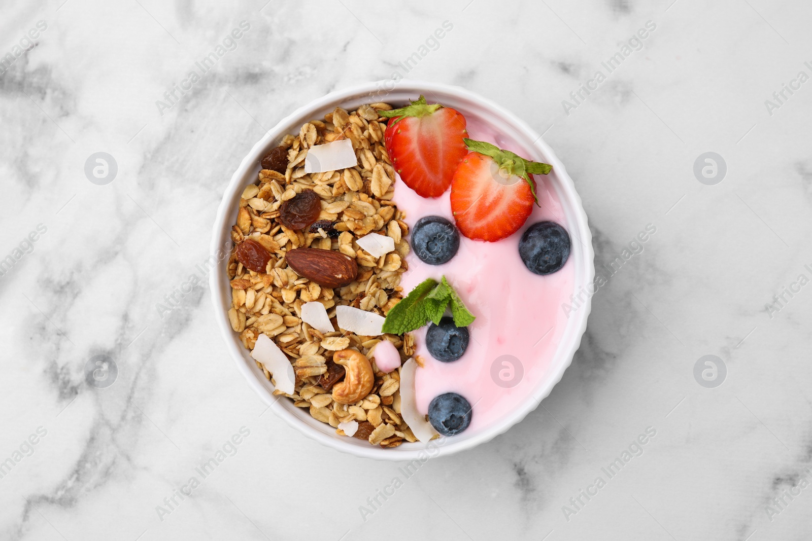 Photo of Tasty granola, yogurt and fresh berries in bowl on white marble table, top view. Healthy breakfast