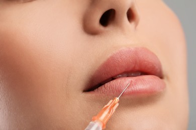 Photo of Young woman getting lips injection on light grey background, closeup. Cosmetic surgery