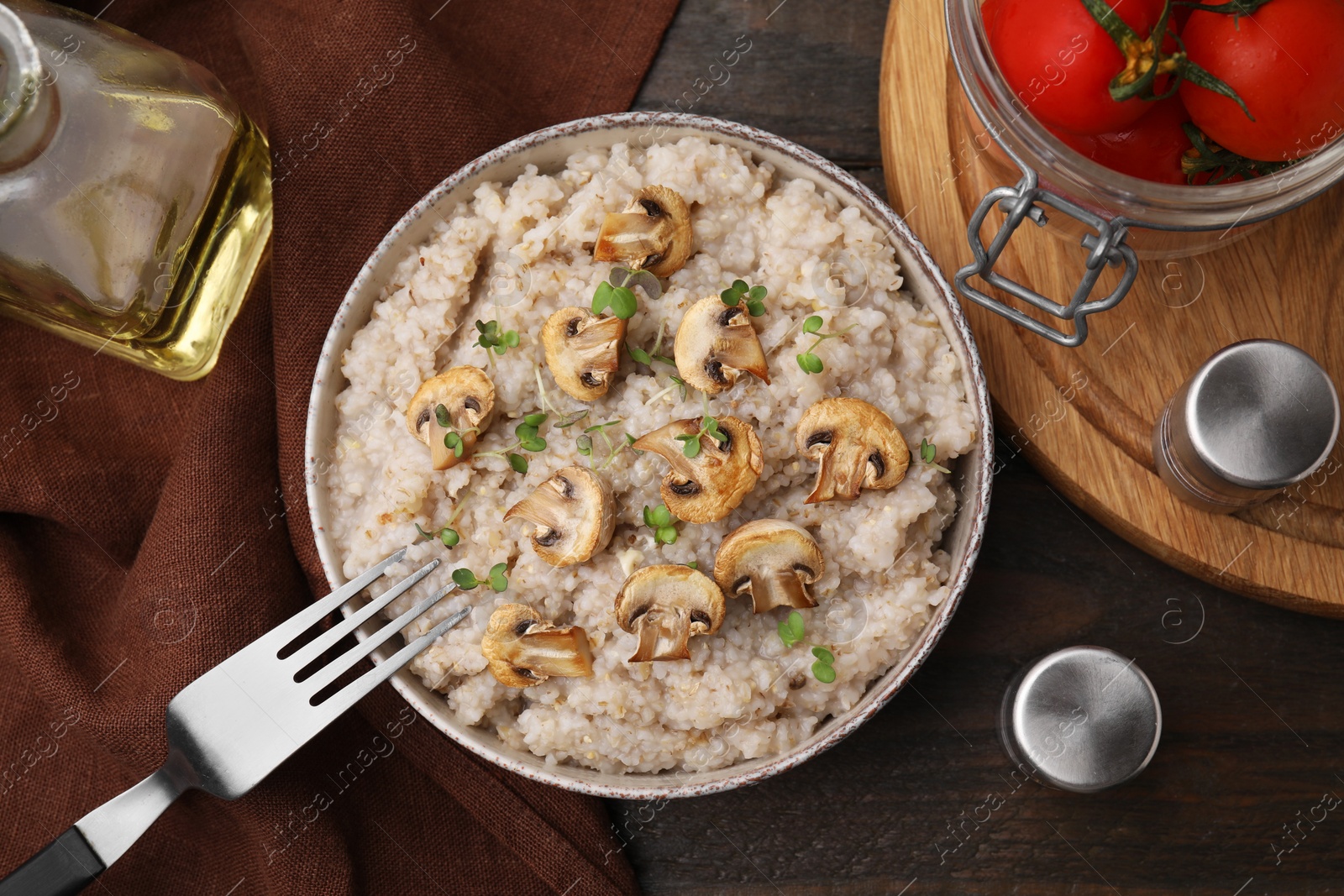 Photo of Delicious barley porridge with mushrooms and microgreens in bowl served on table, flat lay