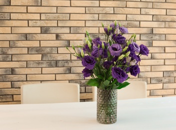 Vase with beautiful flowers on white table against brick wall. Stylish interior