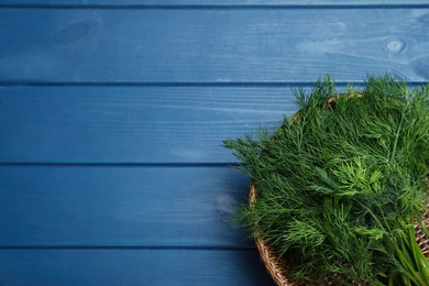 Photo of Fresh dill in wicker basket on blue wooden table, top view. Space for text