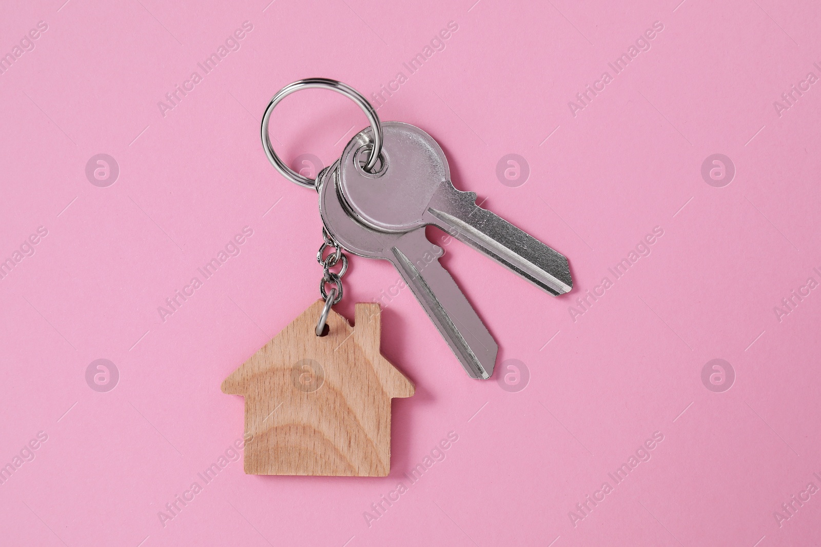 Photo of Metallic keys with wooden keychain in shape of house on pink background, top view