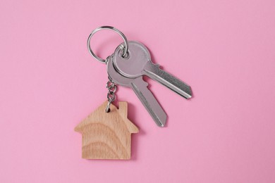 Photo of Metallic keys with wooden keychain in shape of house on pink background, top view