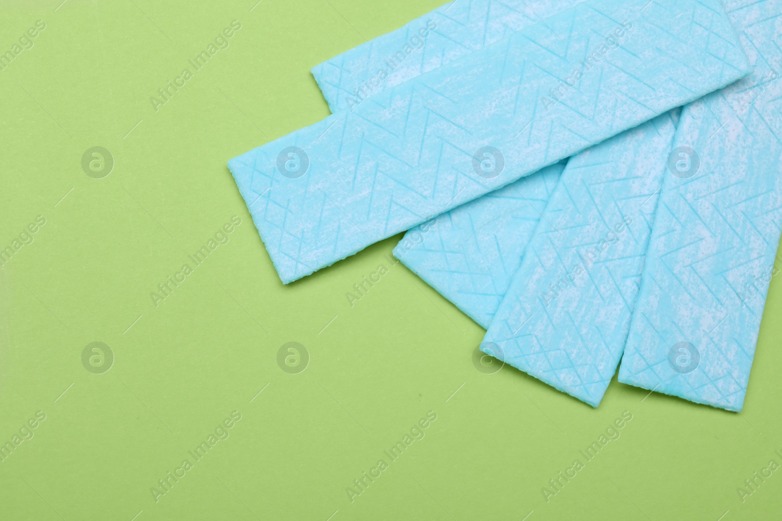 Photo of Many sticks of tasty chewing gum on light green background, flat lay. Space for text