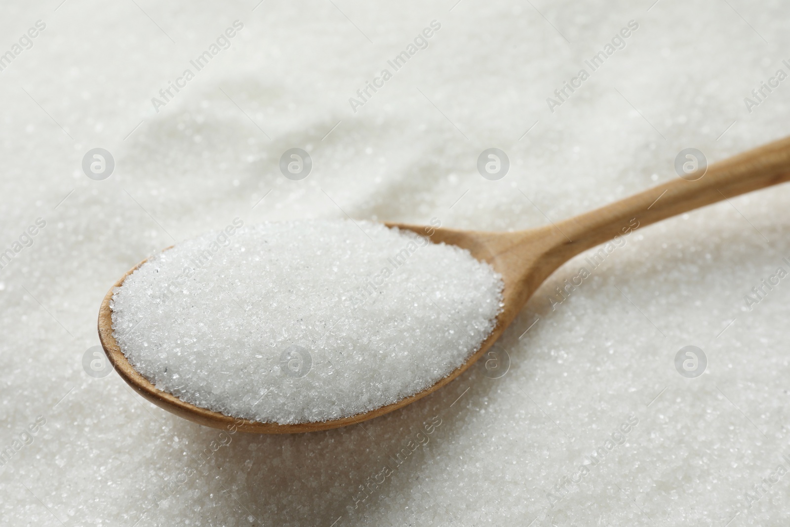 Photo of Wooden spoon on granulated sugar, closeup view