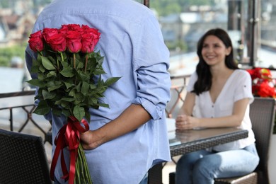 Photo of International dating. Man hiding bouquet of red roses for his beloved woman in restaurant, closeup