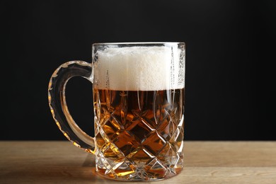 Photo of Mug with fresh beer on wooden table against black background, closeup