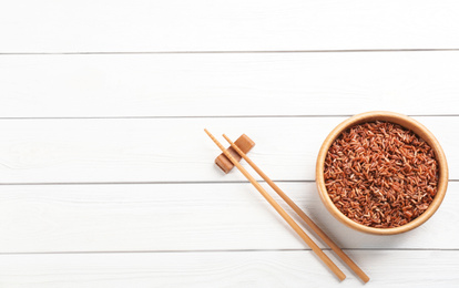 Photo of Tasty brown rice and chopsticks on white wooden table, flat lay. Space for text