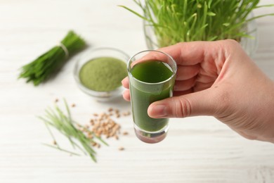 Photo of Woman holding glass of wheat grass drink at white table, closeup