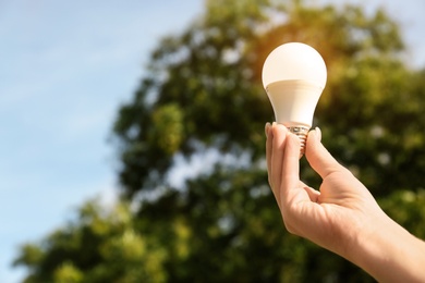 Photo of Woman holding lamp bulb outdoors, closeup. Space for text