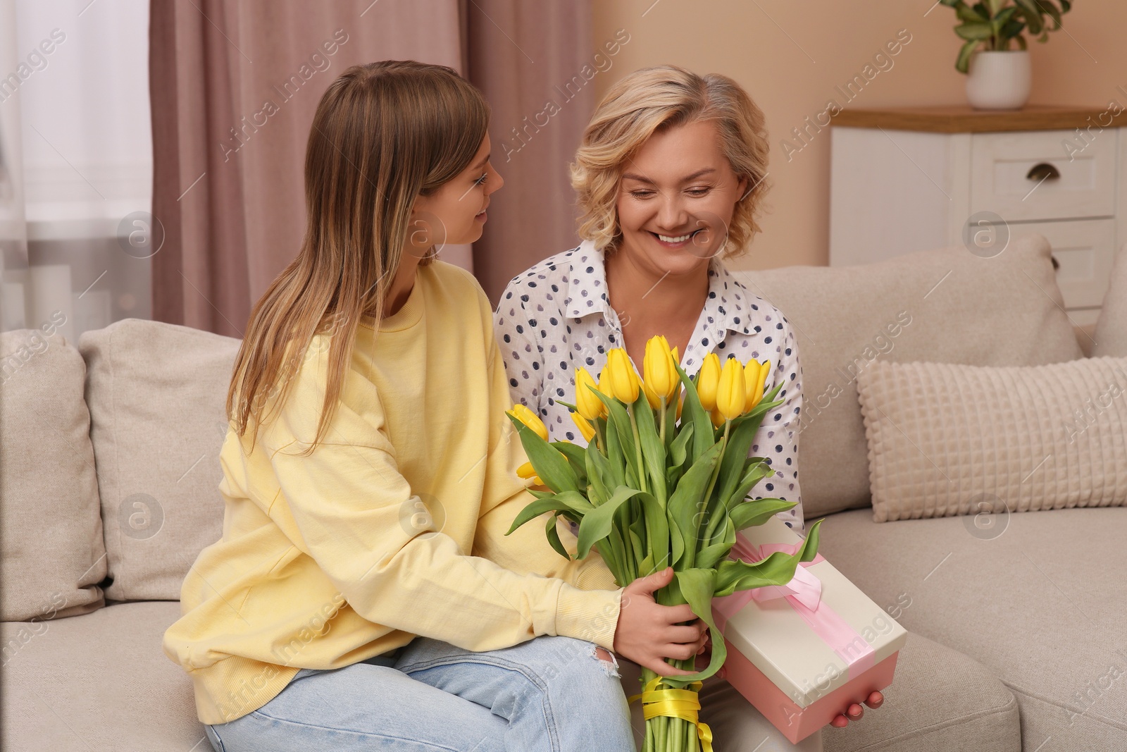 Photo of Young daughter congratulating her mom with flowers and gift at home. Happy Mother's Day