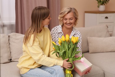 Photo of Young daughter congratulating her mom with flowers and gift at home. Happy Mother's Day