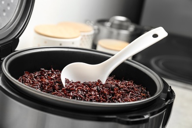 Photo of Modern multi cooker with spoon and boiled brown rice in kitchen, closeup
