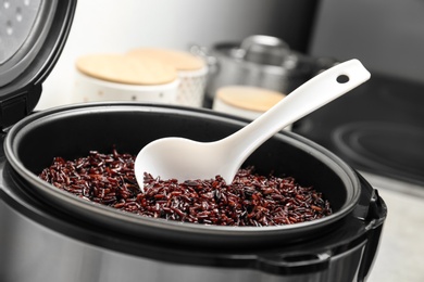 Modern multi cooker with spoon and boiled brown rice in kitchen, closeup