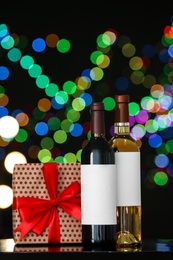 Photo of Gift box with and bottles of wine on table against blurred lights, space for text. Bokeh effect