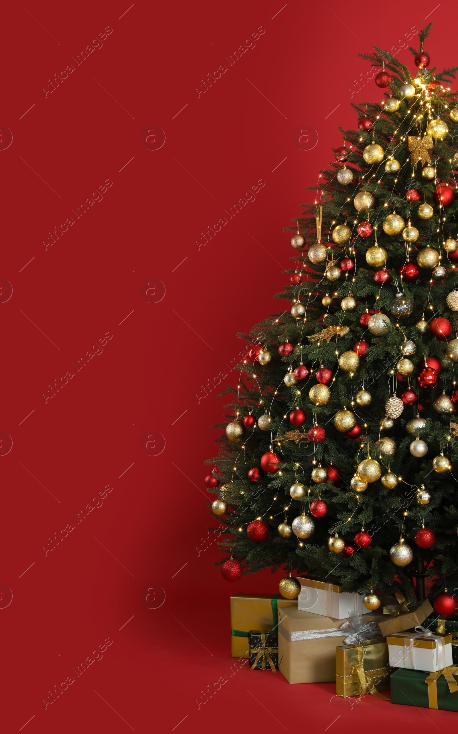 Photo of Beautifully decorated Christmas tree and many gift boxes on red background