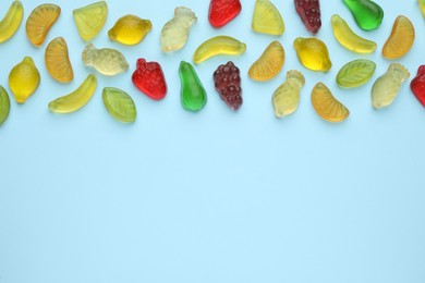 Photo of Tasty jelly candies in shape of different fruits on light blue background, flat lay. Space for text